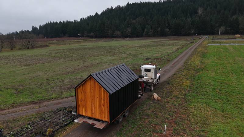 A cedar-and-black shed on the delivery trailer, in a field